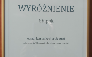 Na zdjęciu widzimy dyplom w ramce z treścią SAMORZĄDOWY LIDER KOMUNIKACJI I PROMOCJI 2022, WYRÓŻNIENIE SŁUPSK OBSZAR KOMUNIKACJI SPOŁECZNEJ ZA KAMPANIĘ "ZOBACZ, ILE KOSZTUJE NASZE MIASTO", Gdynia 19 maja 2022 i podpis Redaktora Naczelnego Dziennika Gazety Prawnej Krzysztofa Jedlaka